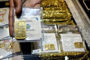 Seorang karyawan menunjukkan emas batangan atau logam mulia Antam di salah satu toko emas di Surabaya, Senin (21/7).