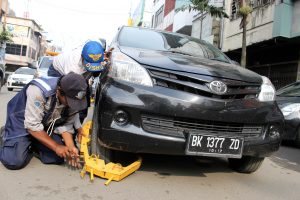 Dua orang petugas Dinas Perhubungan mengunci ban mobil dengan gembok yang diparkir sembarangan di Jalan Cirebon Medan, Sumut, Rabu (12/11). Operasi tersebut bertujuan menertibkan parkir berlapis dengan melakukan penggembokan terhadap kendaraan guna mengantisipasi terjadinya kemacetan arus lalulintas. ANTARA FOTO/Septianda Perdana/Rei/pd/14.